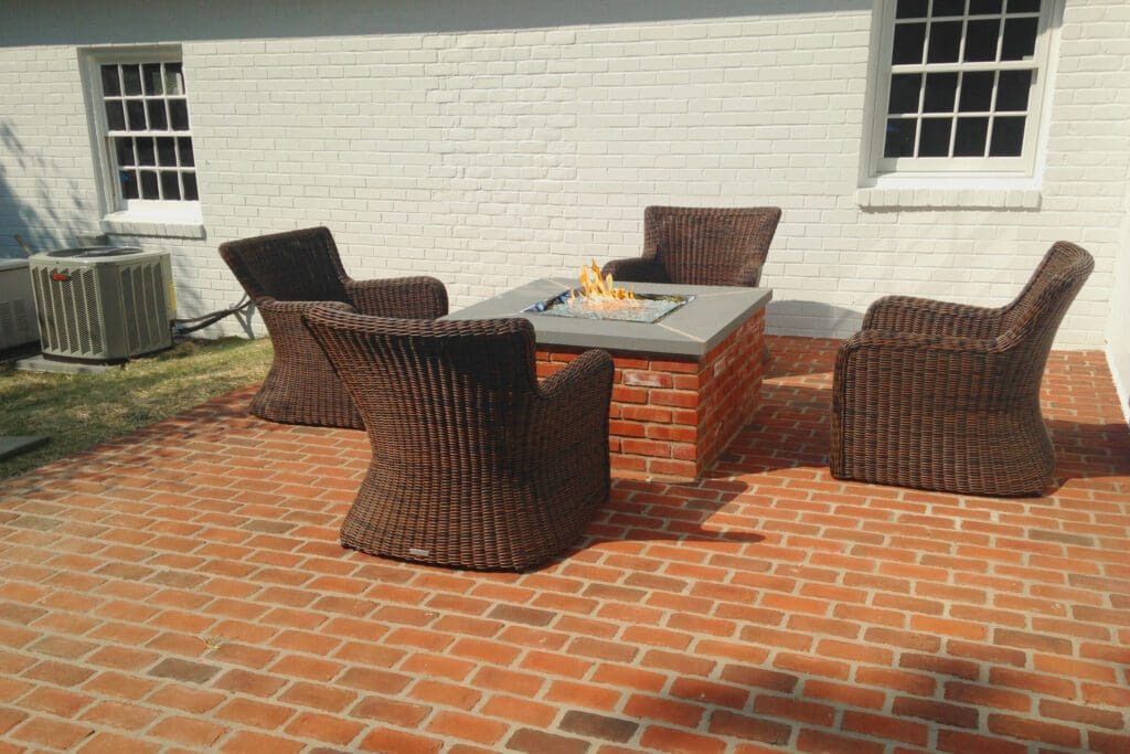 A brick fire pit seamlessly matches the brick patio it's on with wicker chairs surrounding it.