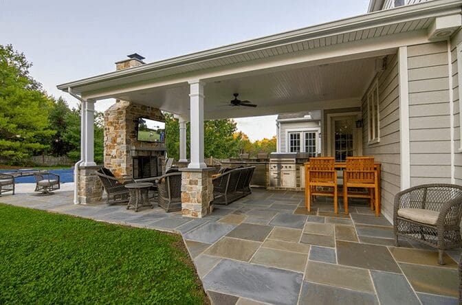 A covered stone patio with a kitchen, seating area, fireplace, and TV.